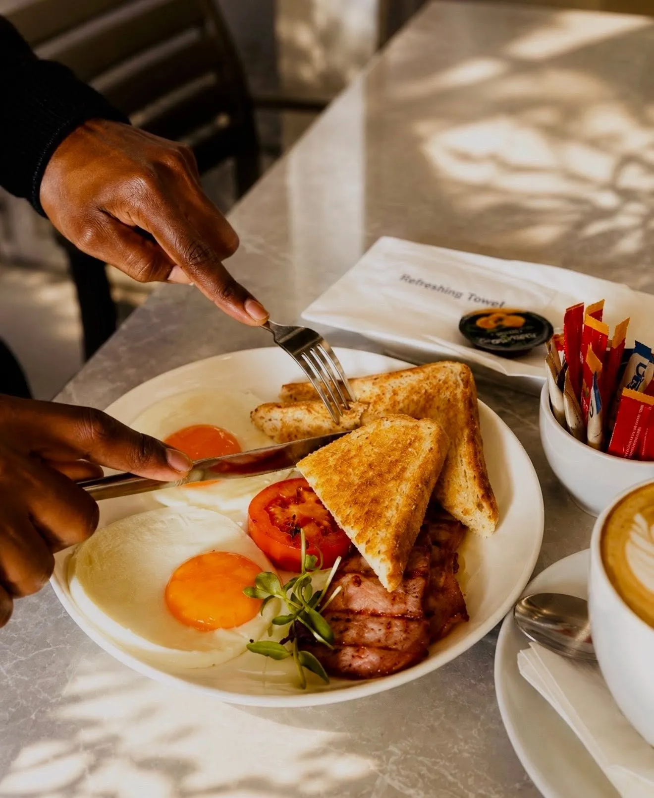 A plate of eggs, bacon and toast being eaten in dappled morning light