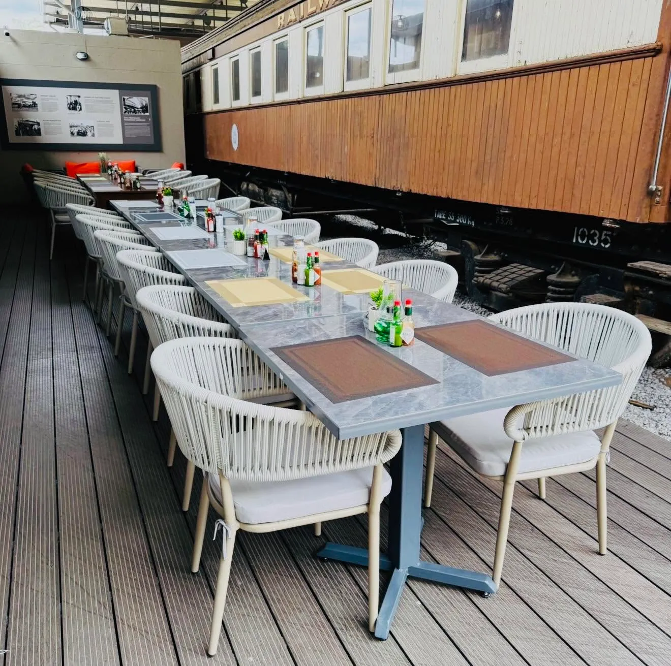 A long banquet table set on the timber deck alongside a railway carriage