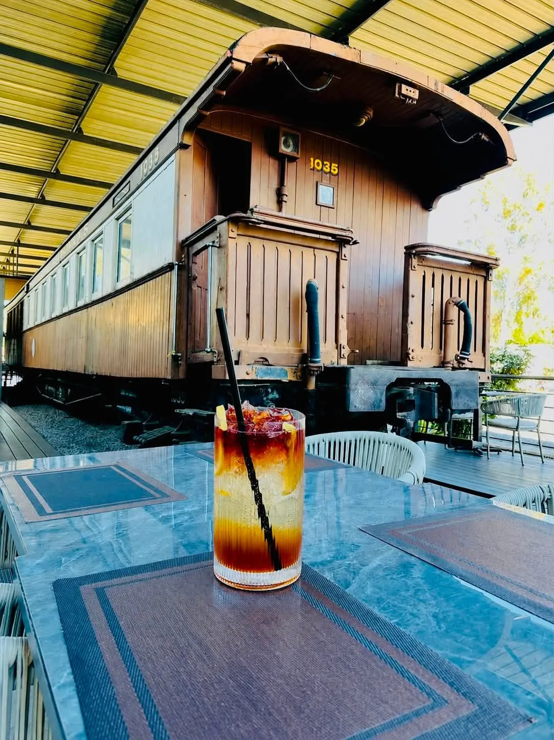 A table on the deck with a drink, a railway carriage behind